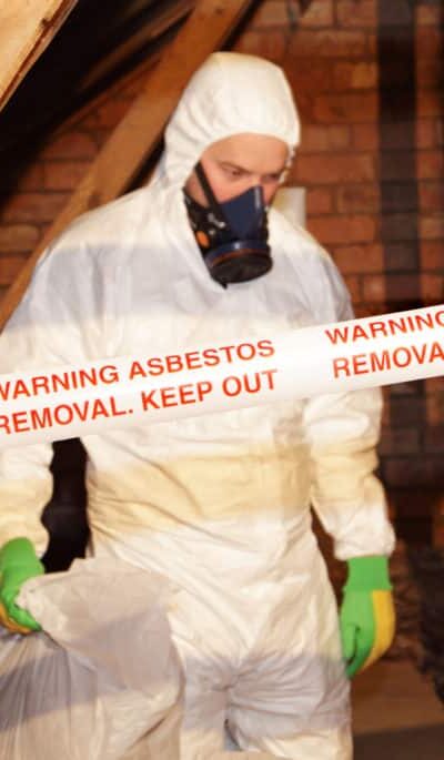 A worker wearing protective clothing while clearing the hazardous substance,asbestos,from an old attic.